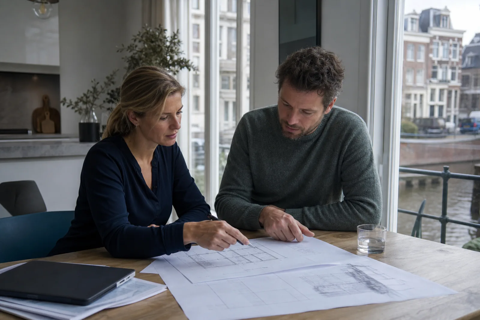 Vergunningsadviseur bespreekt bouwtekeningen met een woningeigenaar aan de keukentafel
