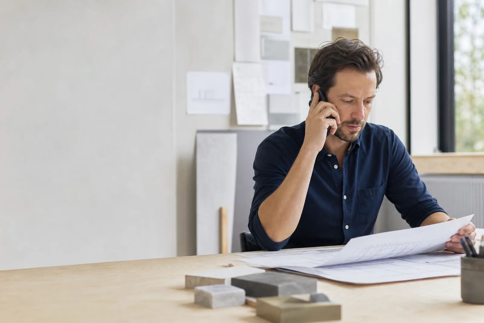 Bouwkundig adviseur beantwoordt telefonisch een vraag bij zijn bouwtekeningen